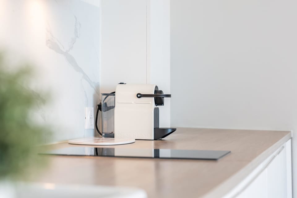 Commencez la journée ici : une Nespresso posée sur un plan de travail en bois clair, dosseret marbre et lumière douce. Préparez un café et savourez la quiétude matinale dans cet espace minimal et chaleureux.