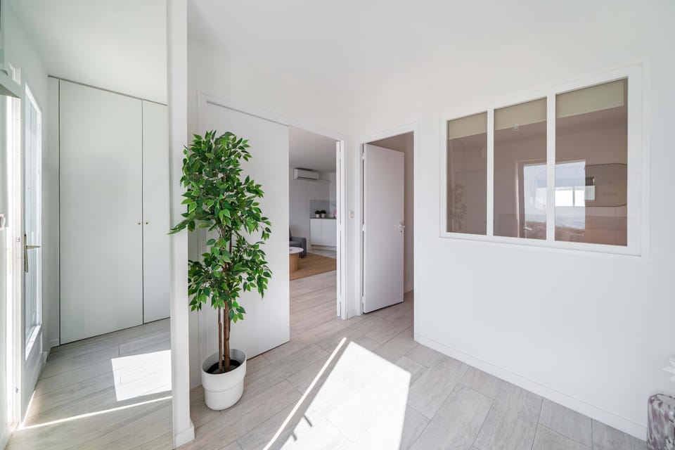 La lumière du matin traverse l'entrée blanche : rangez vos manteaux dans l'armoire encastrée, respirez près du ficus et poussez la porte vers un salon climatisé — simplicité scandinave et douceur accueillante.