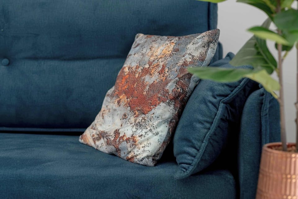 A close-up focus showcases a plush teal cushion paired with a colorful, abstract-patterned throw pillow on the sofa armrest.