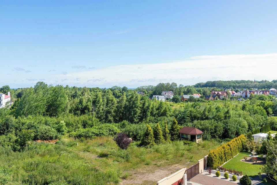 A wide panoramic view from the balcony overlooks an expansive area of lush green fields and trees stretching to the horizon.