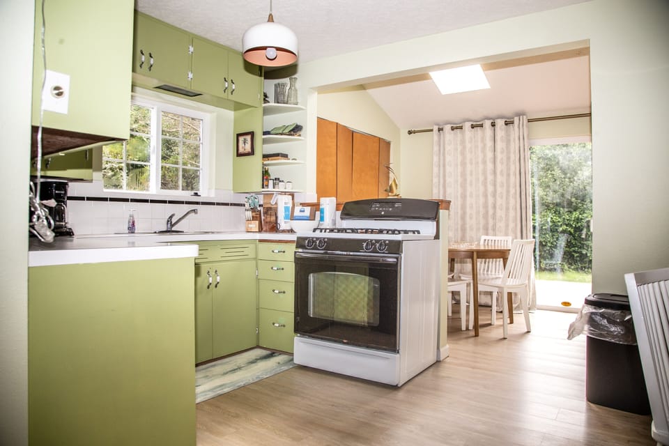 Step into your bright, fully-equipped kitchen with cheerful green cabinetry, modern appliances, and a sunny dining nook where you can enjoy home-cooked meals surrounded by natural light.
