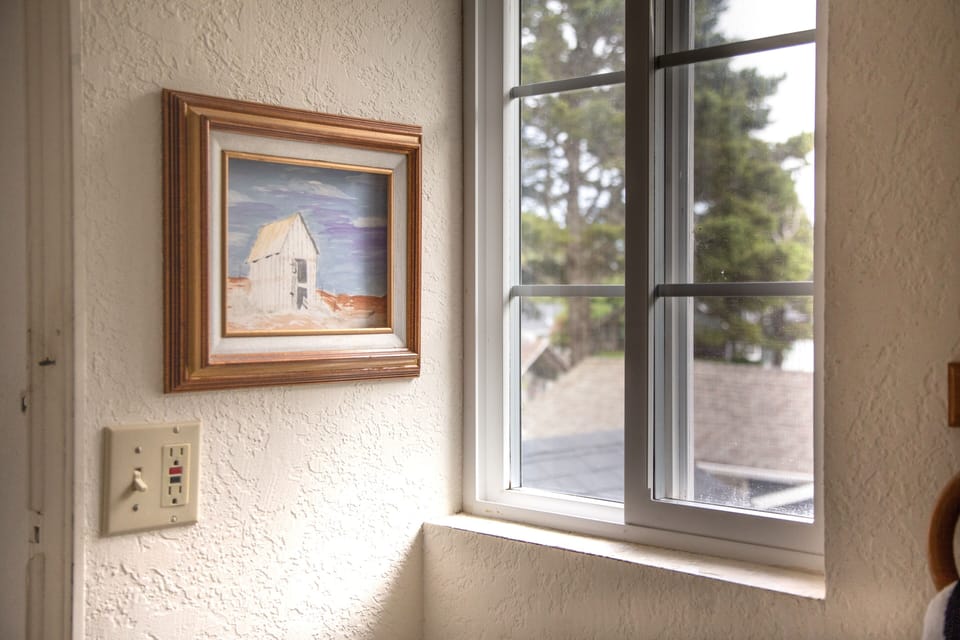 A charming coastal painting brightens the textured wall beside your window, which frames leafy views of the peaceful neighborhood outside.