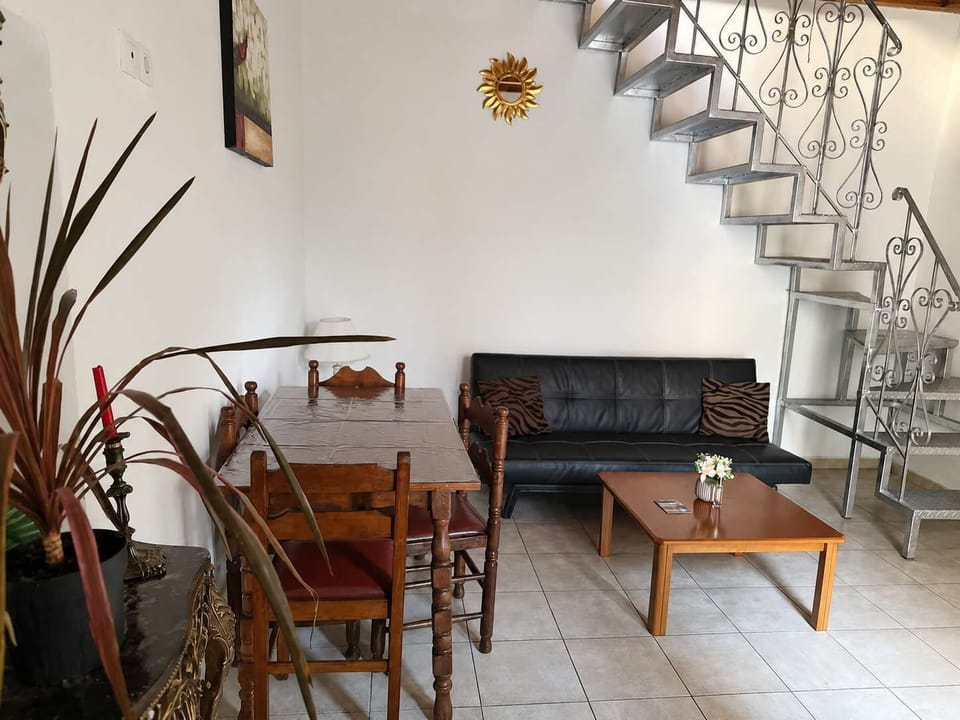 Living and dining area with a classic wooden table, black sofa, coffee table and metal staircase, blending traditional details with a practical and comfortable open-plan layout