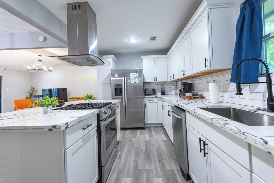 Bright modern kitchen with island, gas range, stainless appliances, coffee maker, toaster oven, and blender.