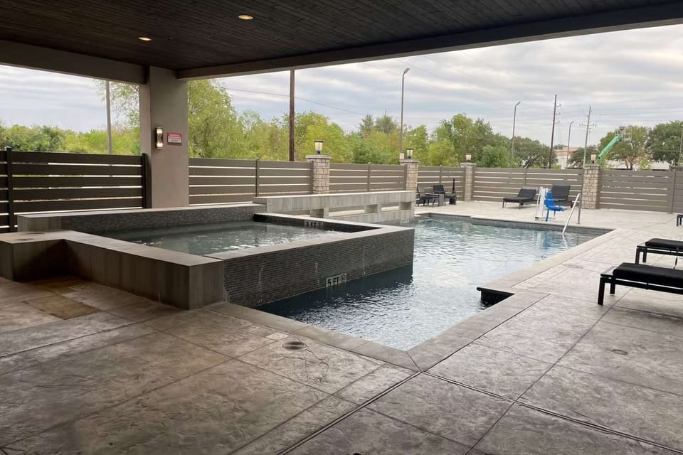 Pool area with spa, lounge chairs, and fenced surroundings