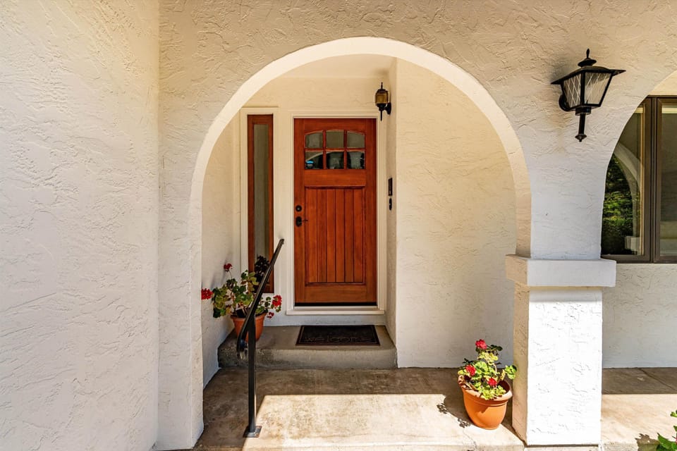 A warm wooden door framed by a charming arched entryway welcomes arrivals, complemented by bright flowers and classic lantern lighting that sets a friendly, inviting tone.