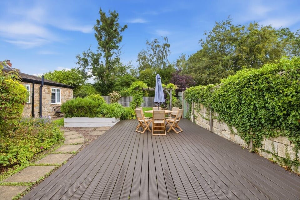 Spacious decked patio with outdoor dining surrounded by mature landscaped gardens