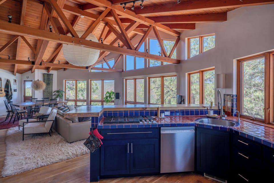 Sunlight floods through floor-to-ceiling windows, illuminating the soaring timber beams and open-concept living space where you'll cook, dine, and relax surrounded by treetop views.