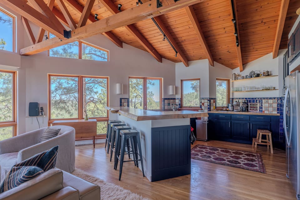 Step into your open-plan haven where soaring wood-beam ceilings and sunlight-filled windows frame stunning mountain views. Cook, gather, and unwind in this beautifully designed space that brings indoor comfort and outdoor beauty together.