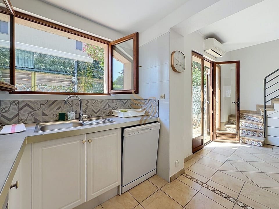 La cuisine fonctionnelle avec évier en inox, lave-vaisselle et une grande fenêtre offrant une vue agréable, idéalement située à proximité de l`entrée et de l`escalier.