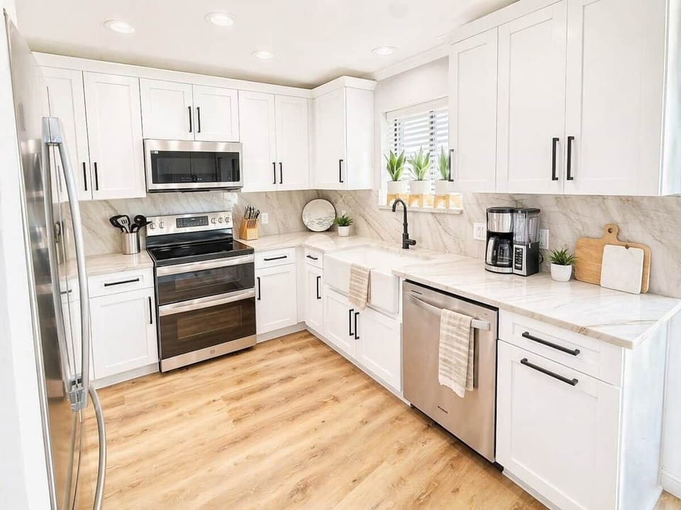 A remodeled, fully stocked kitchen with stainless steel appliances, stunning quartzite countertops and backsplash, farmhouse sink—and a dry bar cocktail corner and a custom stone seating window niche, creating the perfect space to unwind and enjoy!