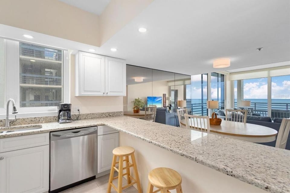 Granite countertop breakfast bar with two wooden stools overlooks dining area and oceanfront balcony.