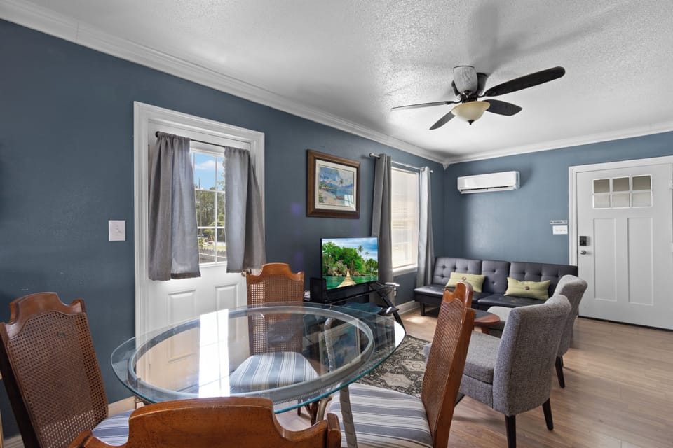 Relax in the open-concept living area, featuring a glass-top dining table, a flat-screen TV, a comfortable futon sofa, and wall-mounted air conditioning.