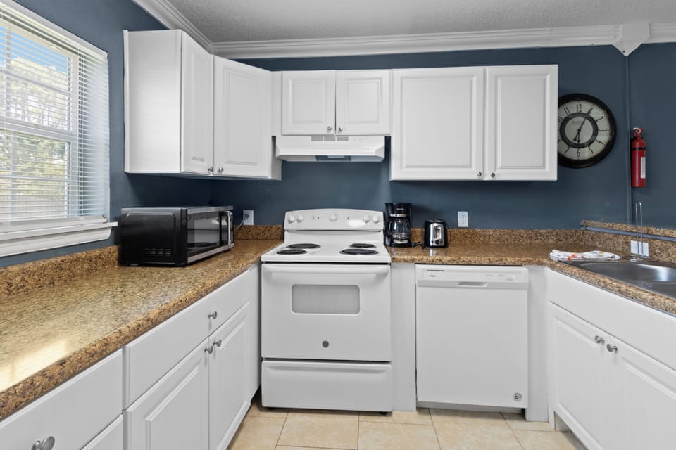 This kitchen setup comes fully equipped with modern white cabinetry, a dishwasher, a coffee maker, and plenty of counter space for meal prep.