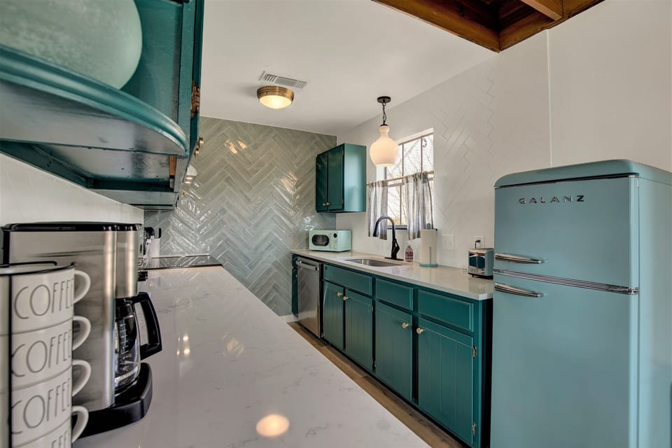 Stylish kitchen with teal cabinets, herringbone tile, a retro mint fridge, and a ready-to-use coffee station—fully equipped for easy meals and morning starts.