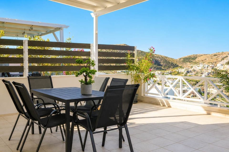 Covered terrace with outdoor dining, shaded seating, and open views across the surrounding Cycladic landscape.