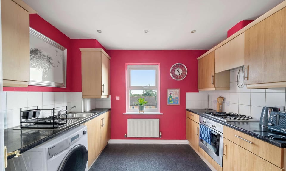 This kitchen features red walls, wooden cabinets, a built-in oven with a gas stove, a kitchen sink, and a front-loading washing machine.