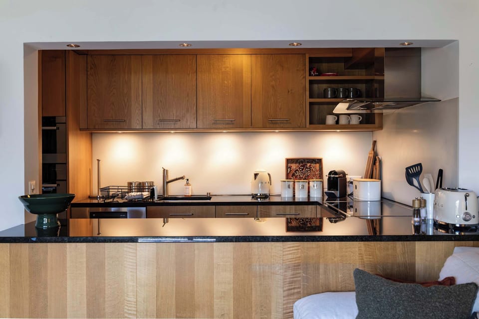 Prepare delicious meals in this fully equipped kitchen, featuring rich wooden cabinetry, sleek dark countertops, under-cabinet task lighting, and small counter appliances.