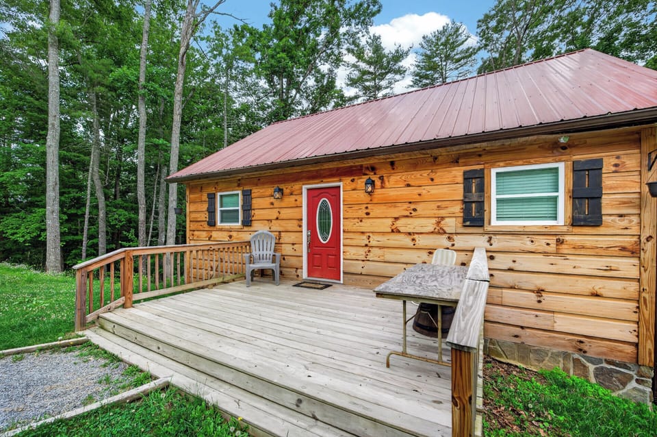 A log cabin with a bright red front door and a spacious wooden porch.