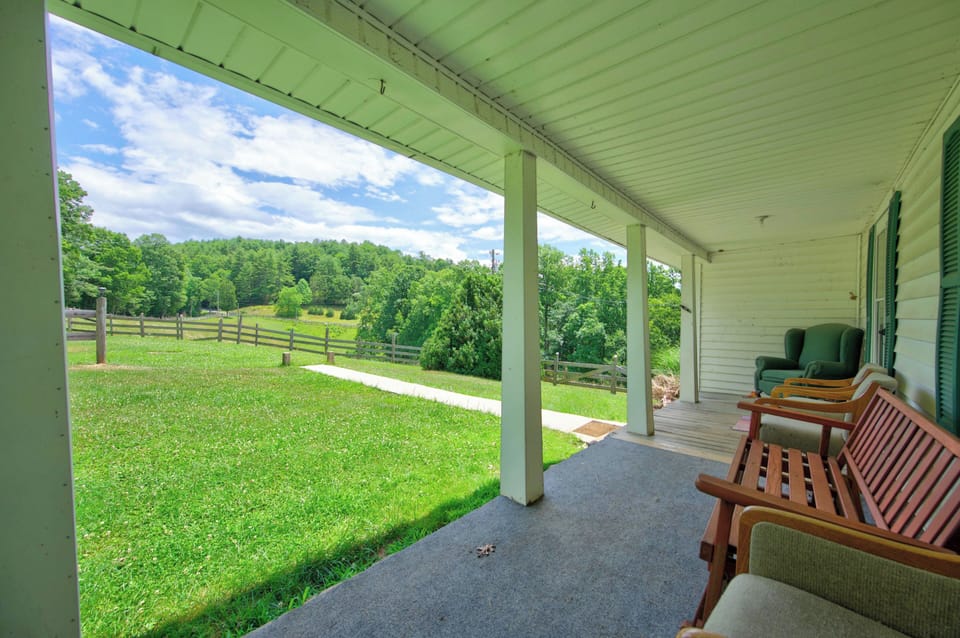 A covered front porch with outdoor seating overlooking a scenic green yard and distant hills.