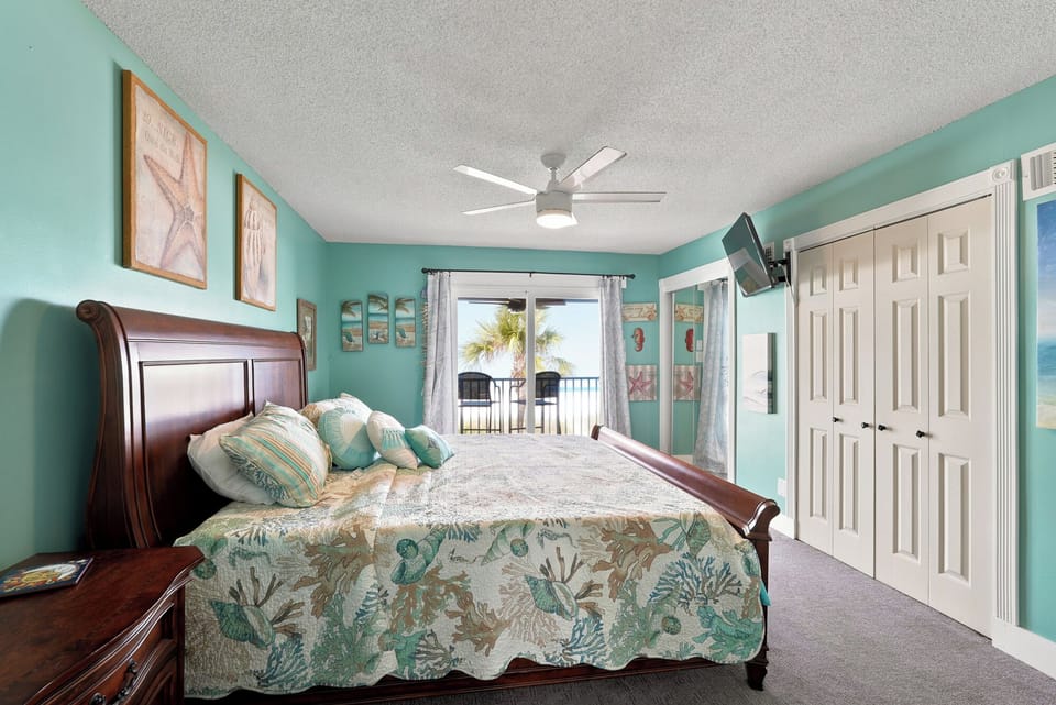 Wake up to coastal charm in your serene bedroom, where soothing aqua walls and beachy decor set the scene. A ceiling fan keeps things cool, while your private balcony beckons with palm-fringed views—pure relaxation awaits.