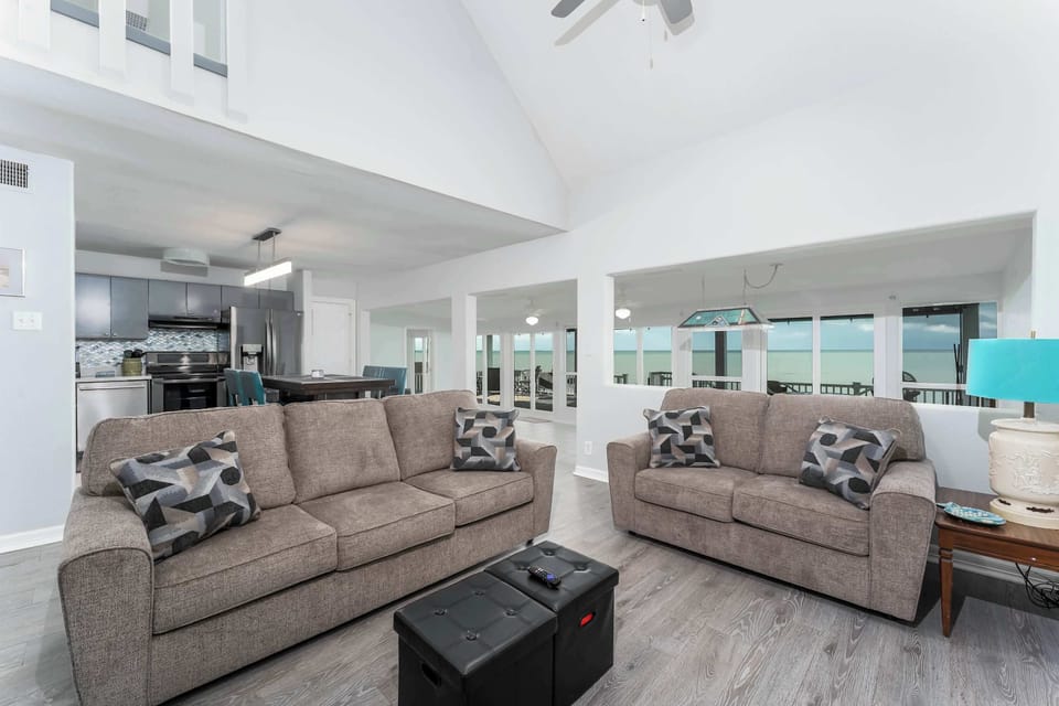 Bright & Spacious Living Room — Relax in the open-concept lounge with plush sofas, vaulted ceilings, and large windows framing breathtaking waterfront views.
