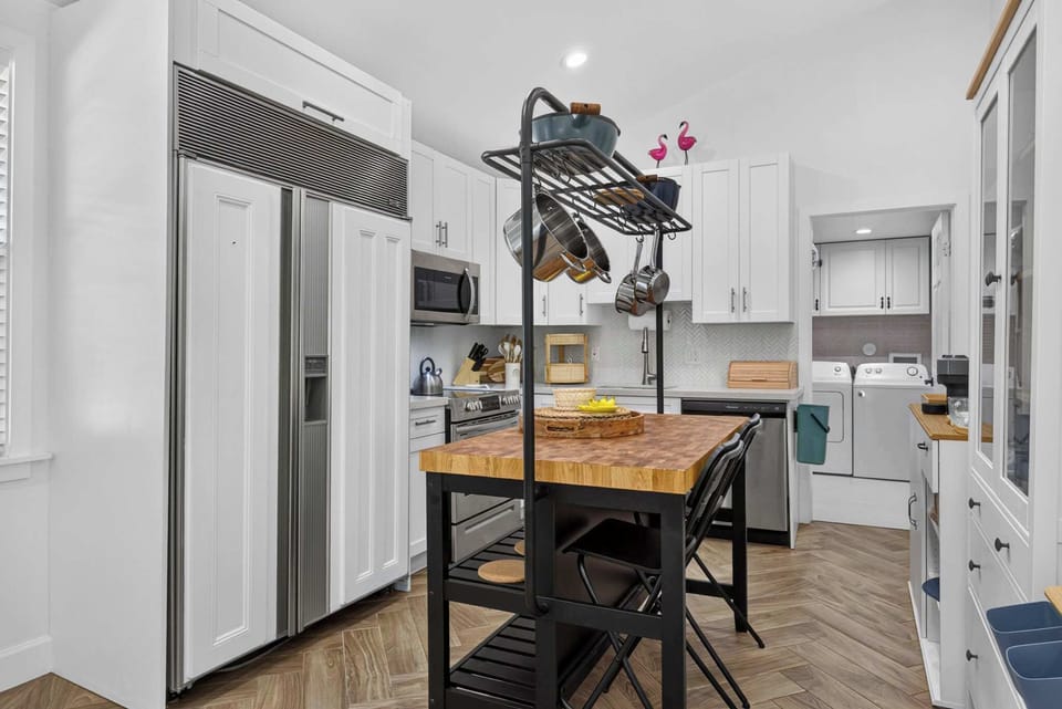 Well-equipped kitchen with a Sub-Zero refrigerator, a butcher block island with seating for two, and a stylish hanging pot rack