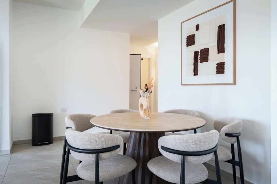 Flowing open-concept zone with round timber table, comfortable dining chairs, seamless sightlines, and bright ambiance.

