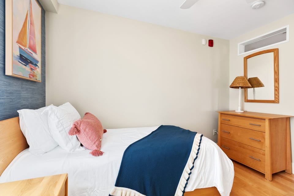 Single bed with fresh linens along with a dresser, Smart TV and mirror