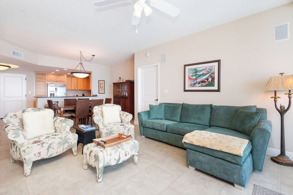 Settle into your open-concept living space, where a plush teal sofa and botanical-print armchairs invite you to unwind after a day of coastal adventures.