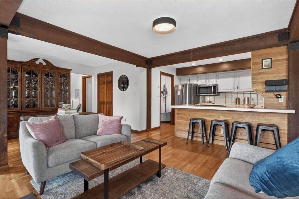 Sink into comfort in your open-concept living space, where rustic beams frame a bright kitchen with sleek appliances and a breakfast bar perfect for morning coffee or evening cocktails.