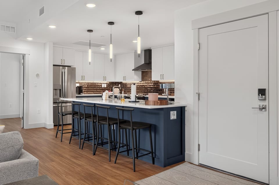 Step into your beautifully designed kitchen featuring sleek white cabinetry, a striking navy island with seating for five, and modern pendant lighting that creates the perfect ambiance for cooking and entertaining.