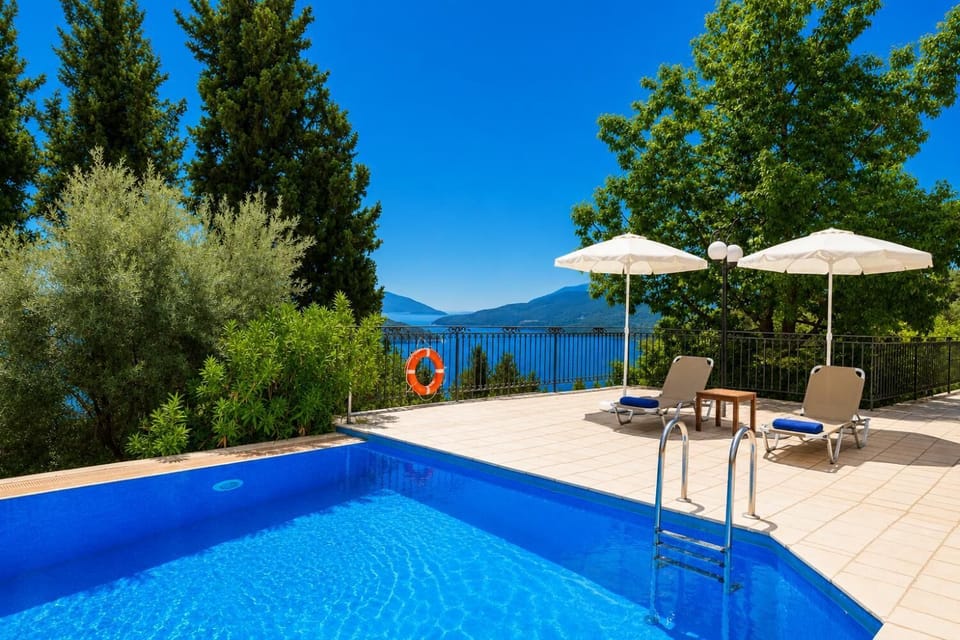 Poolside terrace with sun loungers and umbrellas overlooking a scenic sea bay.