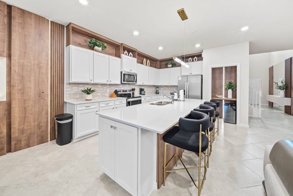 Welcome to a bright, stylish kitchen with sleek white cabinetry and warm wooden accents. The spacious island, topped with elegant bar stools, is perfect for casual meals or enjoying your morning coffee in the natural light.