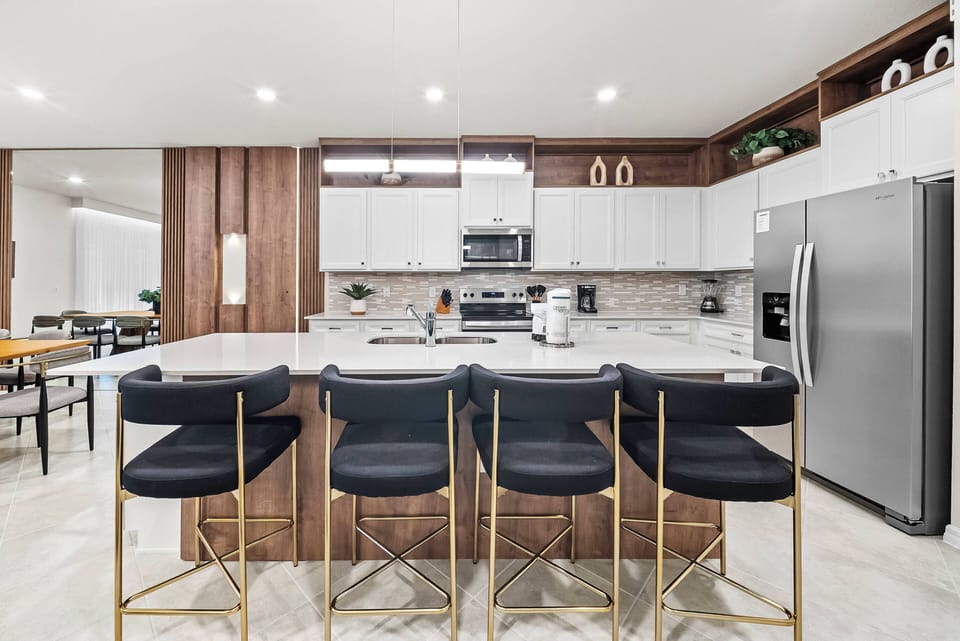 Enjoy culinary delights in this stylish kitchen with sleek white cabinets and warm wood accents. The spacious island and chic black bar stools invite gatherings, while modern appliances make cooking a breeze.