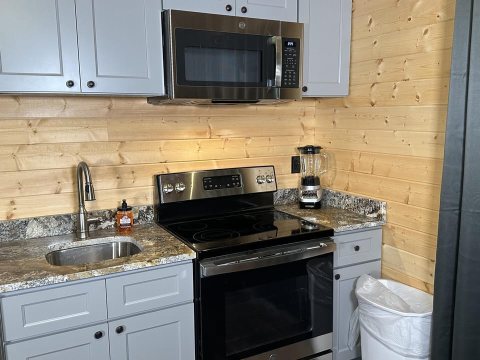 Light wood plank walls frame the kitchen corner with gray cabinetry, granite countertops, and stainless steel appliances.
