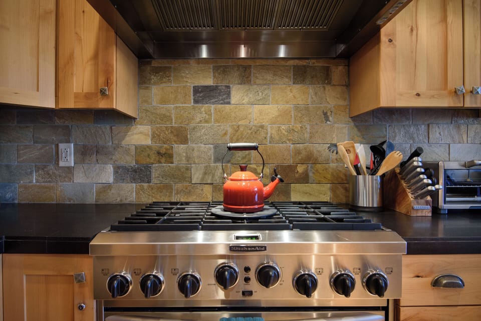 Chef-style gas range with rustic stone backsplash and warm wood cabinetry