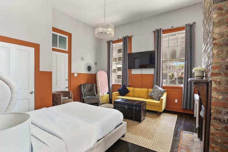 Spacious bedroom with high ceilings, large windows, and a seating area with TV. Filled with natural light and designed for comfort, blending historic details with modern touches.