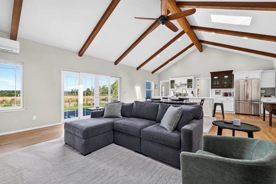 A full view of the expansive living area with the large sectional couch and vaulted wood-beamed ceiling.