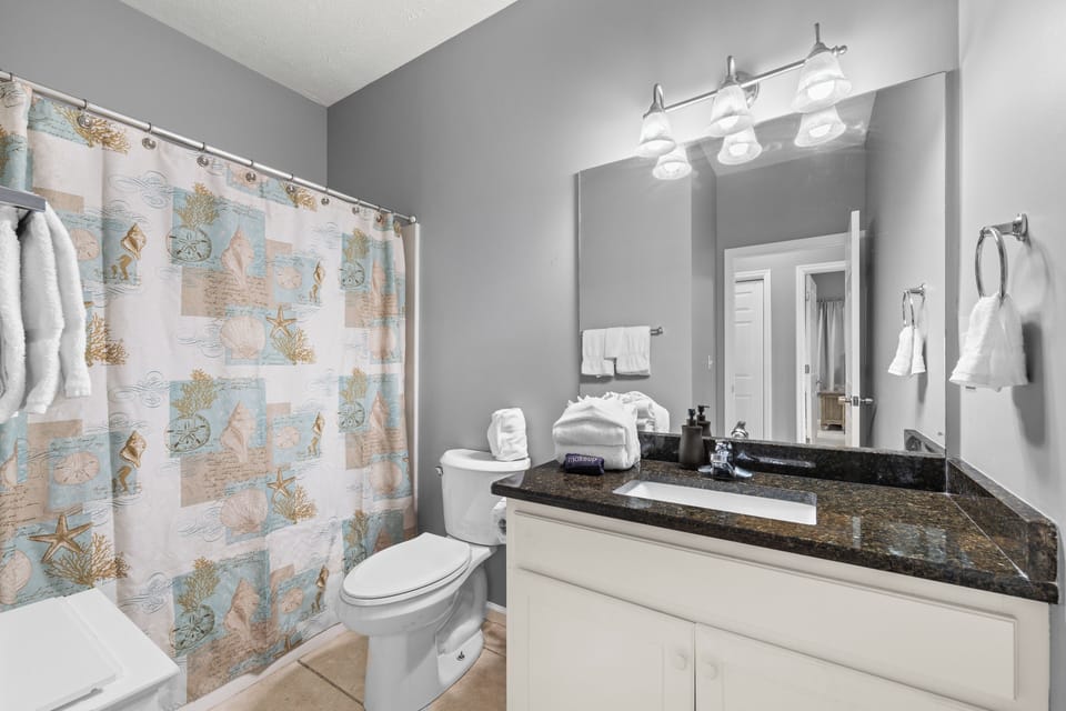 Your private bathroom features coastal charm with fresh towels, granite countertops, and a playful ocean-themed shower curtain that sets the perfect beach getaway mood.