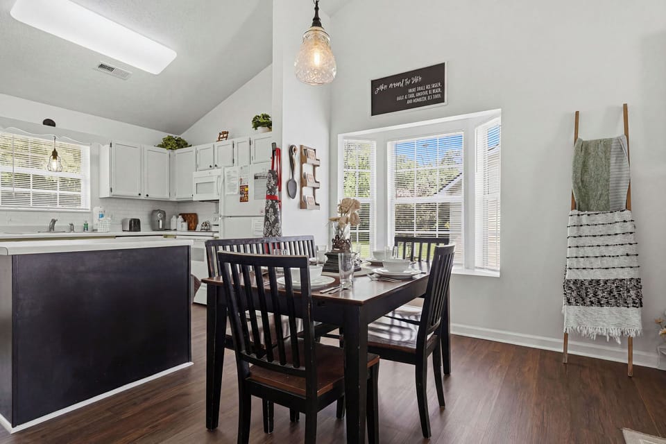 Gather around the welcoming dining table in this bright, open-concept space where natural light streams through large windows. The modern kitchen with sleek cabinetry stands ready for your home-cooked meals.