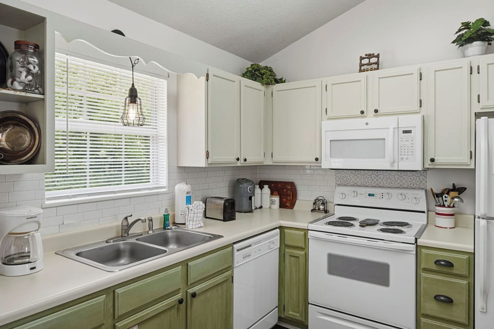 Picture yourself brewing morning coffee in your fully equipped kitchen, where natural light streams through the window, highlighting the charming two-tone cabinetry and modern appliances ready for your culinary creations.