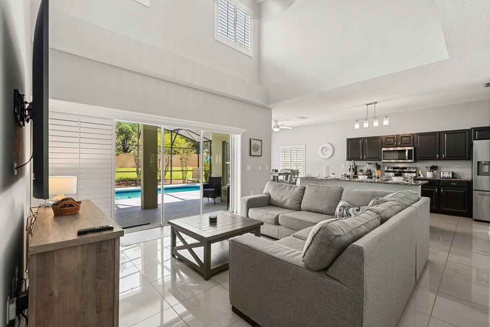 Gather in the bright, open-concept living room with soaring ceilings, comfortable seating, and direct access to the private pool patio.