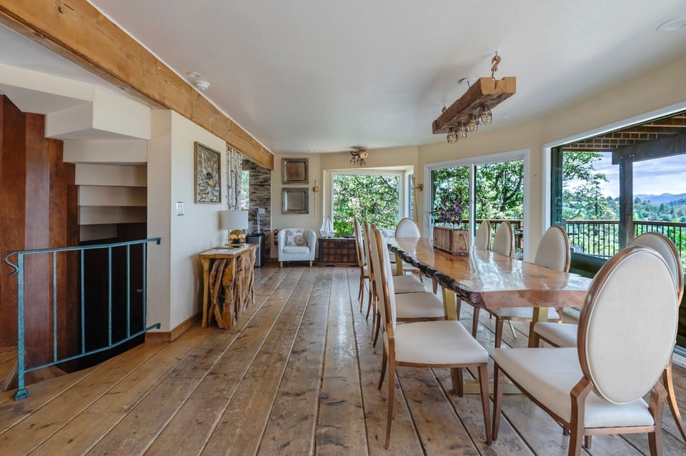 Dining space featuring a long live-edge table, wide-plank flooring, and scenic outdoor views.