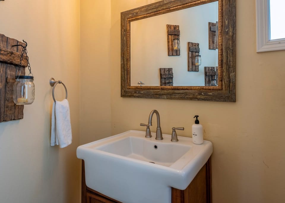 A bathroom vanity features an apron-front sink and a rustic framed mirror.