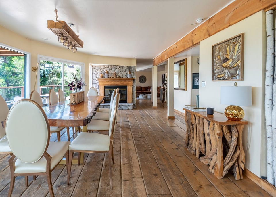 A dining space with wide-plank wood floors, a live-edge table, and a stone fireplace.