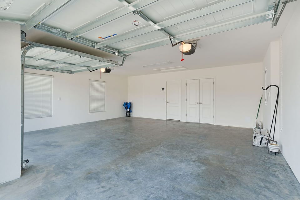 Spacious garage with exposed track lighting, smooth concrete floors, and interior access door leading to the home.