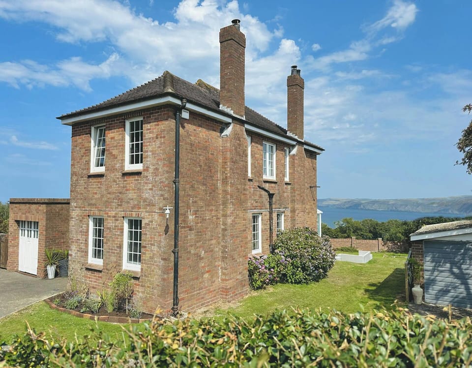Two-storey brick house with chimneys and white-framed windows beside a lawn