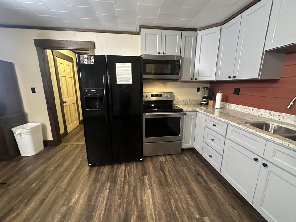 Kitchen features stainless steel appliances, white cabinets, granite countertops, and reddish wood plank backsplash.