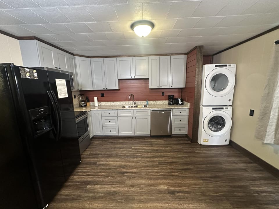 Kitchen with white cabinetry, granite countertops, black refrigerator, and stacked white washer and dryer on wood-look flooring.